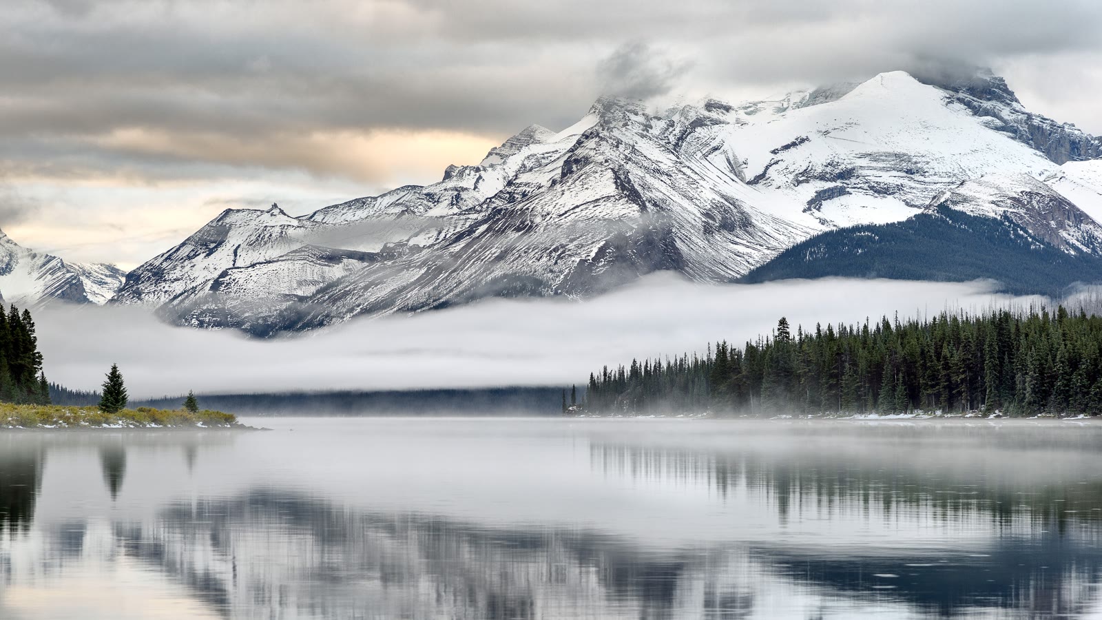 A snow-capped mountain reflecting in a still alpine lake at sunrise